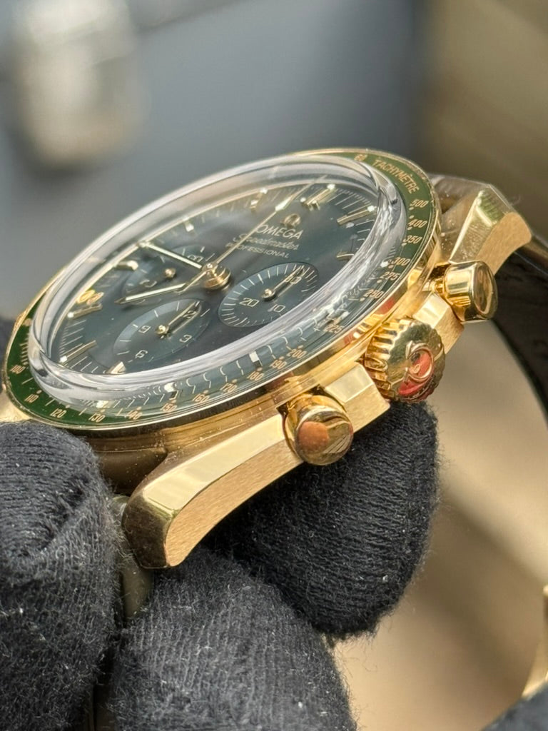 A close-up view of a gloved hand holding a gold Omega Speedmaster Professional "Moonshine" 310.63.42.50.10.001 wristwatch with a dark dial and chronograph features by Omega.