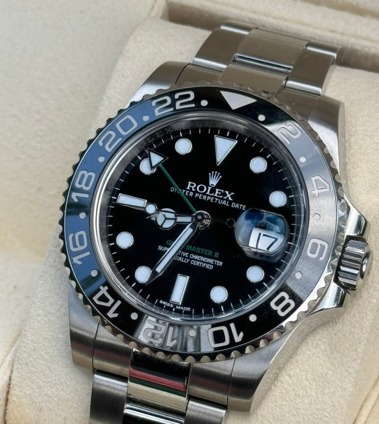 Close-up image of a Rolex GMT-Master II 116710LN watch featuring a black and blue ceramic bezel, luminescent hour markers, and a date window, all driven by precise automatic movement. The elegant timepiece is displayed on a beige surface.