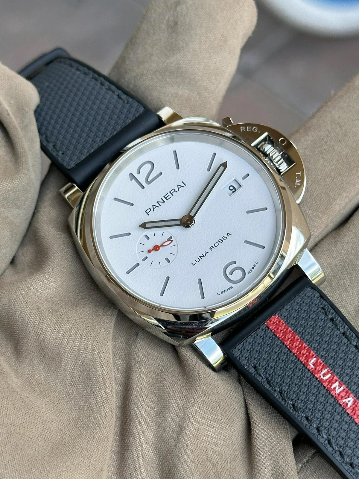 A hand wearing a glove holds a Panerai Luminor Due Luna Rossa PAM01381 with a white dial, black leather strap, and red accent. Perfect for sailing enthusiasts, this timepiece features an automatic P.9010 movement, displaying time, date, and a small seconds sub-dial.