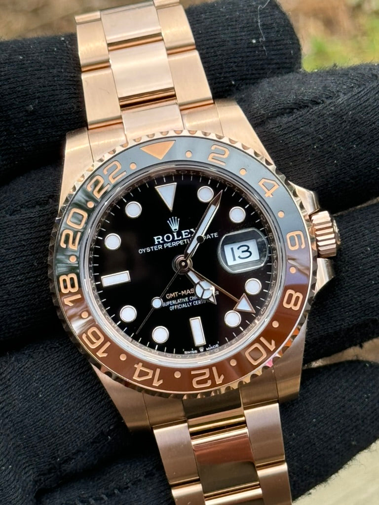 A Rolex GMT-Master II 126715CHNR "Rootbeer" watch with a black dial, Rootbeer two-tone bezel, and Everose Gold bracelet, displayed on a black gloved hand.