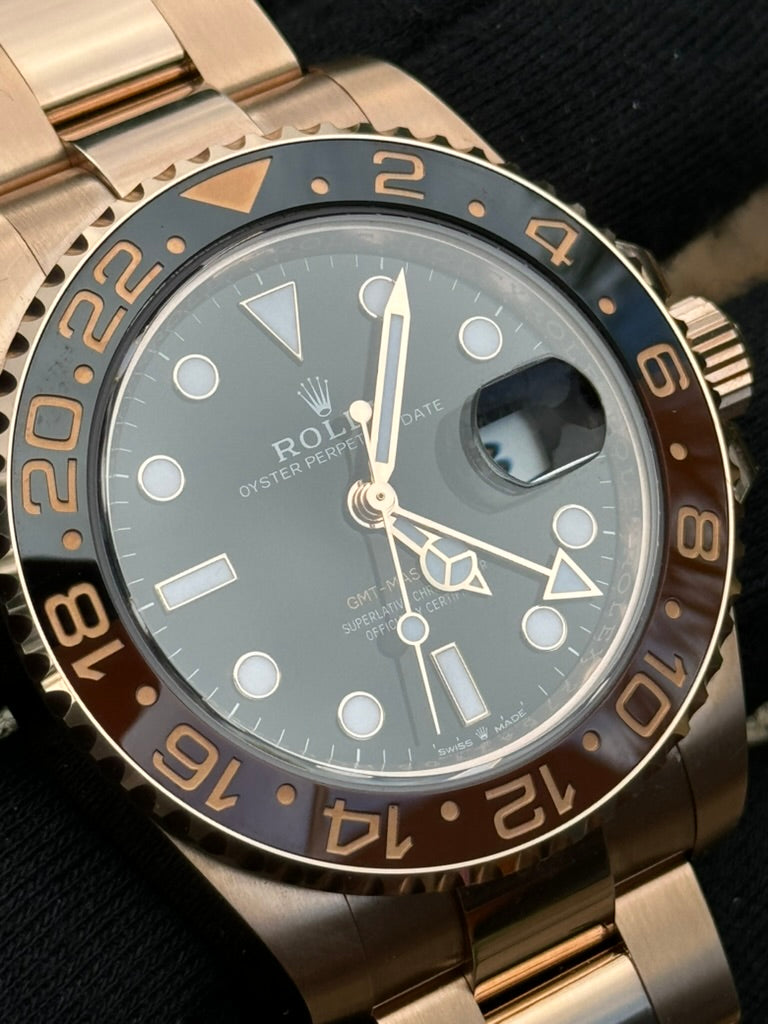 A stunning rose gold Rolex GMT-Master II 126715CHNR "Rootbeer," also known as the Rootbeer, features a black and brown bezel. It displays time, date, and an additional 24-hour time with luminous hands and markers. The watch rests elegantly on a black surface.