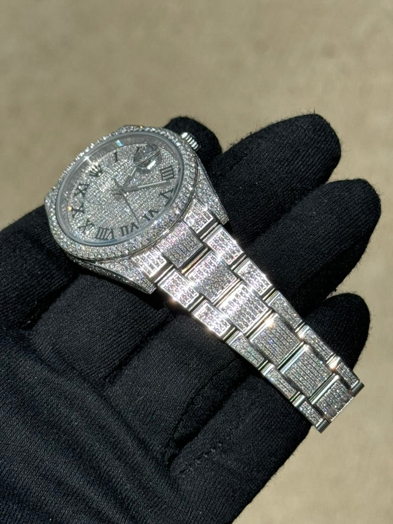 A gloved hand holding a Rolex Datejust 126300 "Bust Down" adorned with diamonds on the dial, bezel, and bracelet.