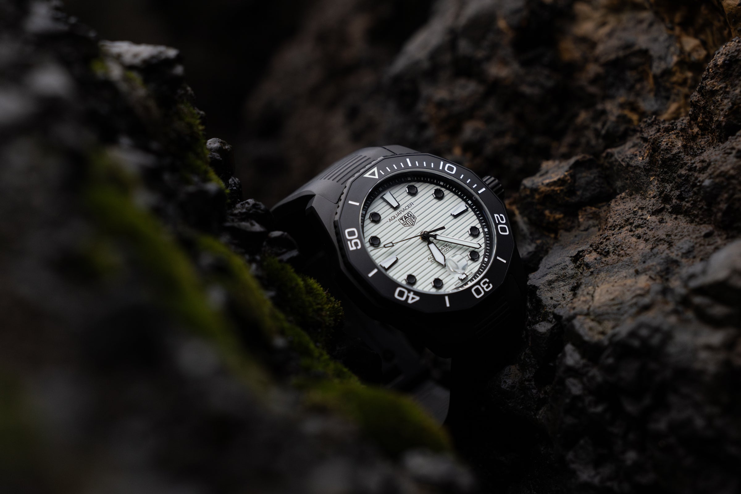 A black Aqaracer watch with a white watch face sitting in a black and brown rock crevice.