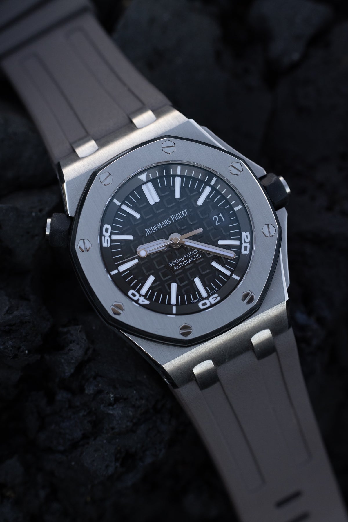 A silver Audemars Piguet watch with a gray band sitting on volcanic rock.